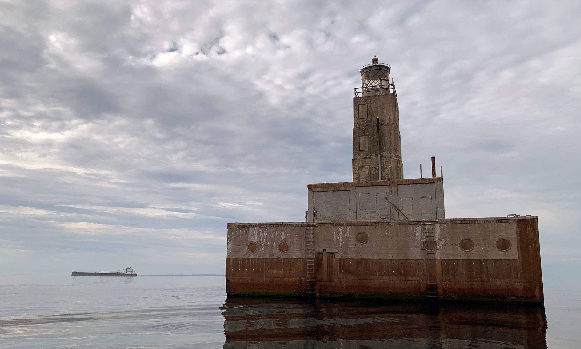 Lansing Shoals Light Station rising from the waters of northeastern Lake Michigan, with a freighter visible on the horizon under dramatic clouds